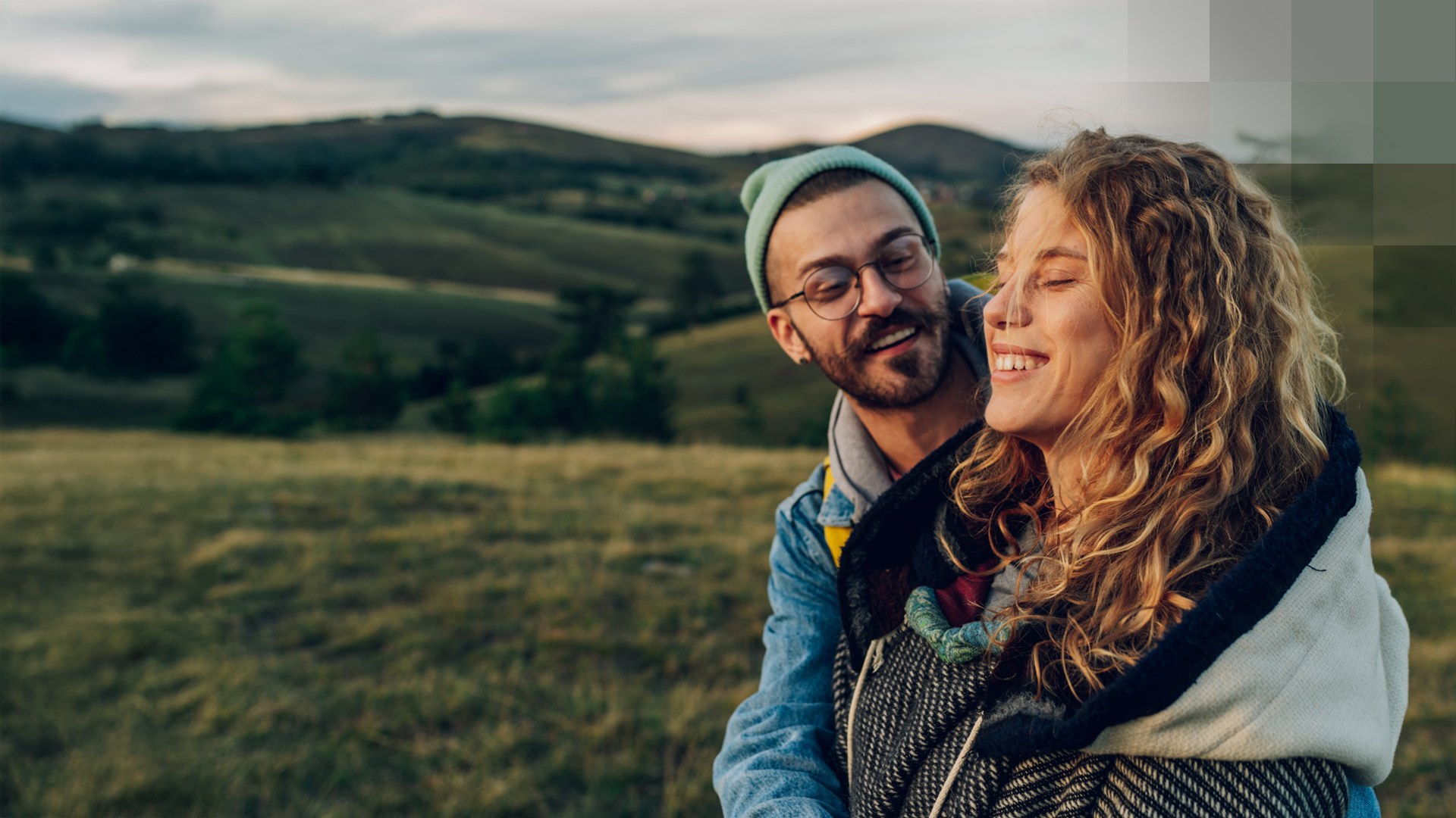 Un jeune couple se tient dehors dans la nature, se serre dans les bras et est heureux d’être en bonne santé grâce au modèle HMO.